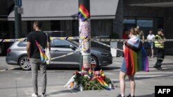 A woman with a progress flag stands at a makeshift memorial at a crime scene, June 25, 2022, in the aftermath of a shooting outside pubs and nightclubs in central Oslo killing two people, injuring 21.