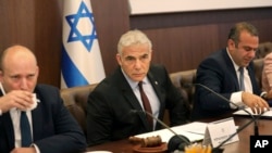 Israeli caretaker Prime Minister Yair Lapid, center, sits next to former Prime MInister Naftali Bennett, left, as he chairs the first cabinet meeting days after lawmakers dissolved parliament, in Jerusalem, July 3, 2022.