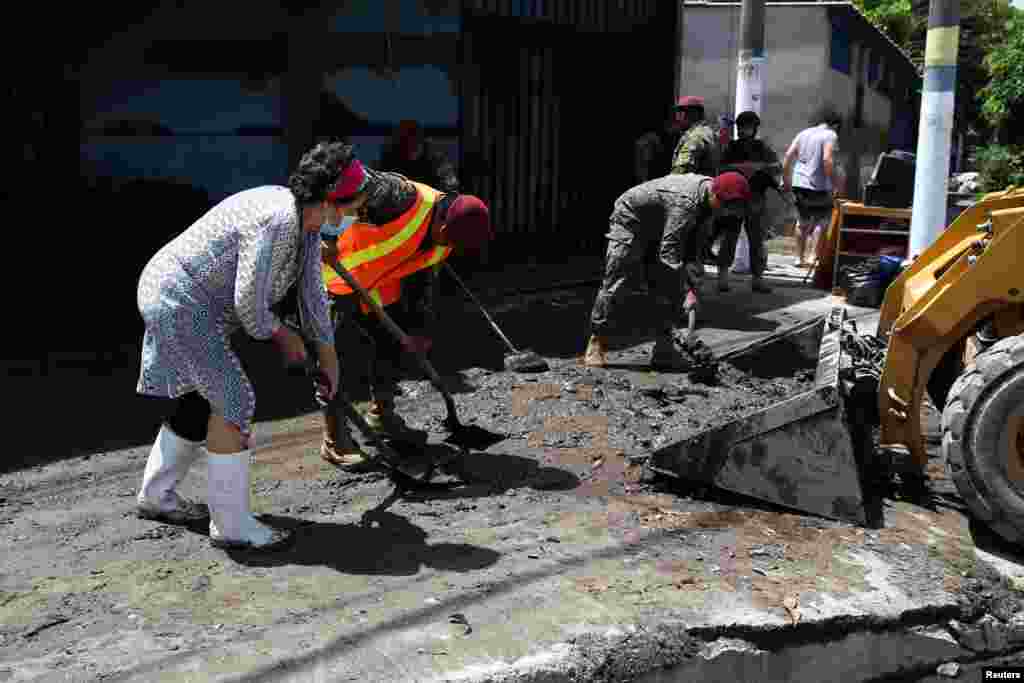 Una mujer y soldados limpian el lodo de la calle después de la tormenta tropical Bonnie, en Ilopango, El Salvador, el 3 de julio de 2022.