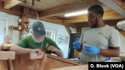 Volunteer Rob Dutton, left, helps apprentice Deion Smalls while they work together on a boat at the seaport center. (Deborah Block/VOA)