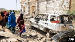 FILE - Women walk next to a destroyed house and car after an explosion set off by al-Shabab militants in Mogadishu, Somalia, Feb. 16, 2022. Al-Shabab has long been fighting to dislodge the central government. One of its most recent attacks occurred June 17, 2023, in Adado.