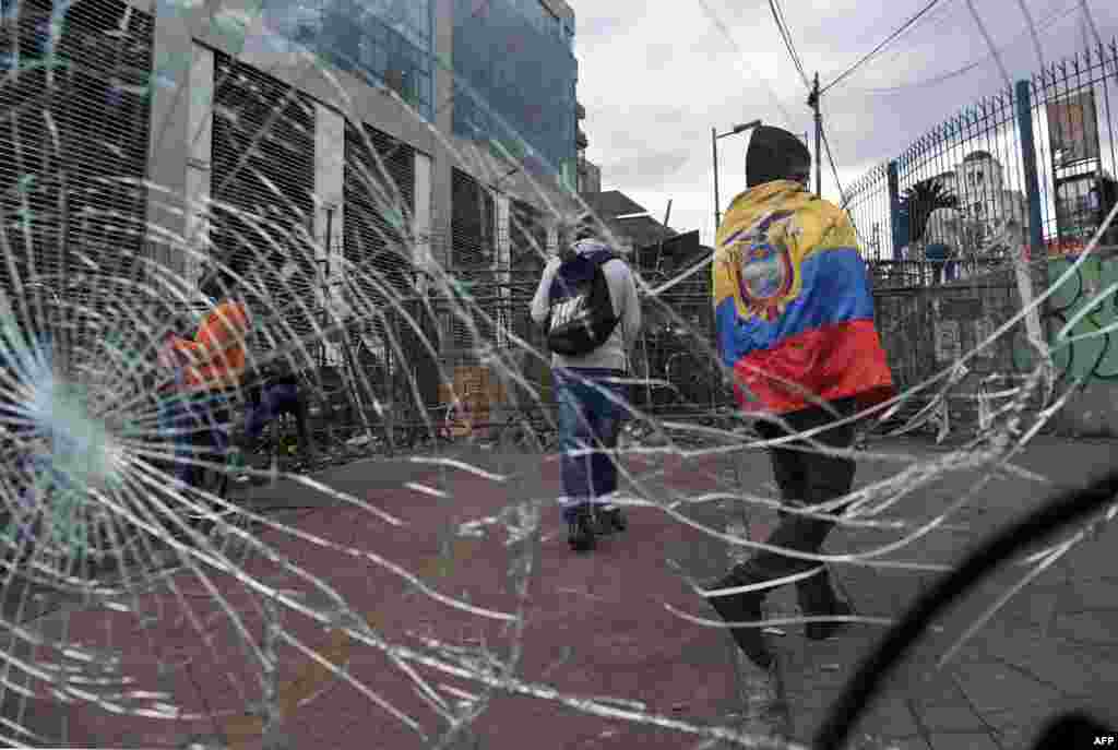 Un indígena envuelto en una bandera nacional ecuatoriana pasa junto a una ventana rota colocada cerca de una barricada en los alrededores del edificio de la Asamblea Nacional en Quito.