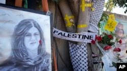 FILE: Yellow tape marks bullet holes on a tree and a portrait and flowers create a makeshift memorial, May 19, 2022, where Palestinian-American Al-Jazeera journalist Shireen Abu Akleh was killed in the West Bank city of Jenin.