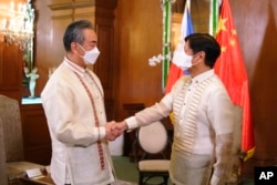 In this photo provided by the Malacanang Presidential Photographers Division, Philippine President Ferdinand Marcos Jr., right, greets Chinese Foreign Minister Wang Yi as the arrives for a courtesy call at the Malacanang Presidential Palace in Manila, Philippines on Wednesday, July 6, 2022. (Malacanang Presidential Photographers Division via AP)