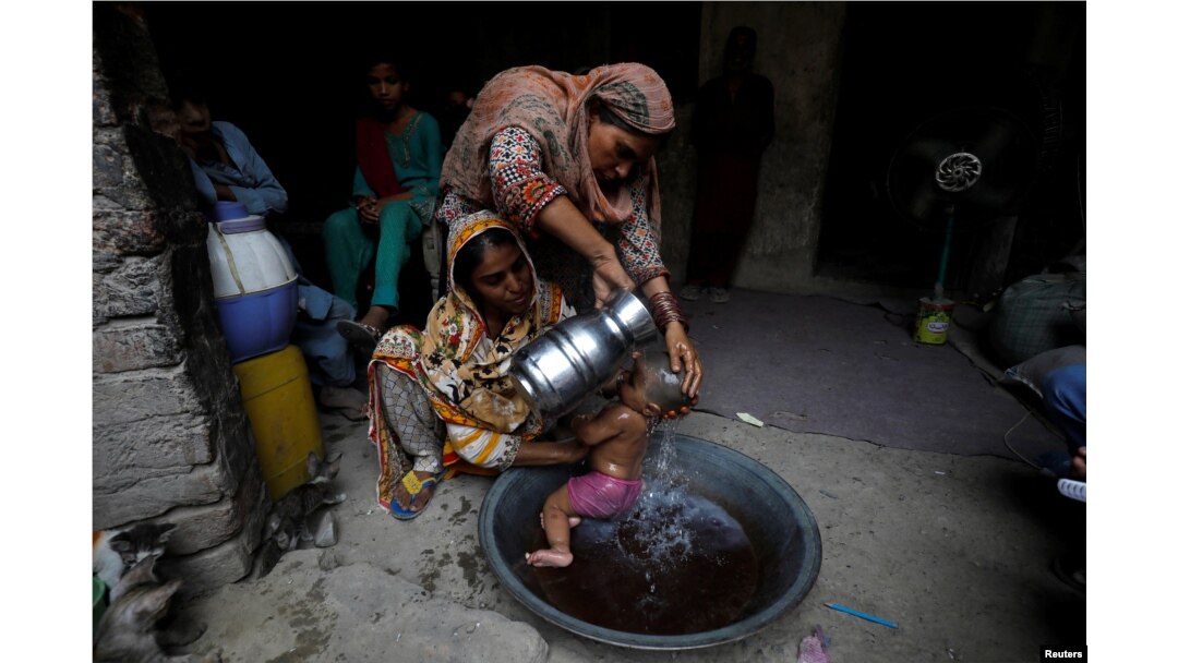 Rehmat, 30, membantu Razia, 25, memandikan putrinya yang berusia enam bulan, Tamanna, untuk mendinginkan tubuh saat gelombang panas, di Jacobabad, Pakistan, 15 Mei 2022. (REUTERS/Akhtar Soomro)