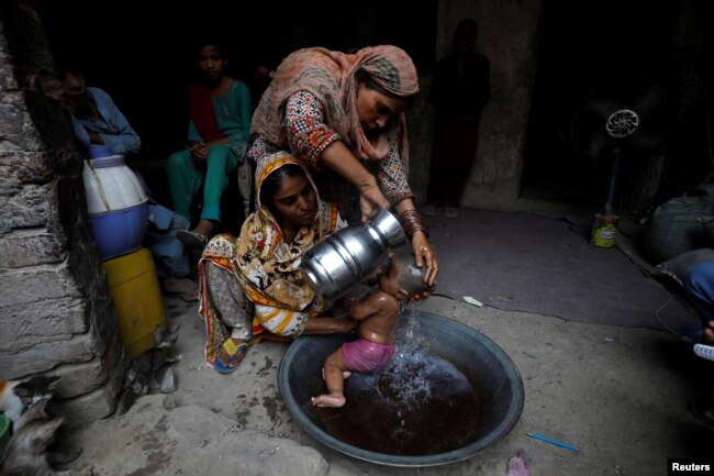 Rehmat, 30, helps Razia, 25, bathe her six-month-old daughter Tamanna to cool off during a heatwave, in Jacobabad, Pakistan, May 15, 2022. (REUTERS/Akhtar Soomro)