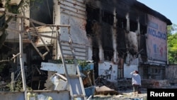 A woman stands next to a building damaged by shelling at a local market in Donetsk, Ukraine, June 19, 2022. 