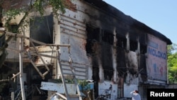 A woman stands next to a building damaged by shelling at a local market in the course of Ukraine-Russia conflict in Donetsk, Ukraine, June 19, 2022. 