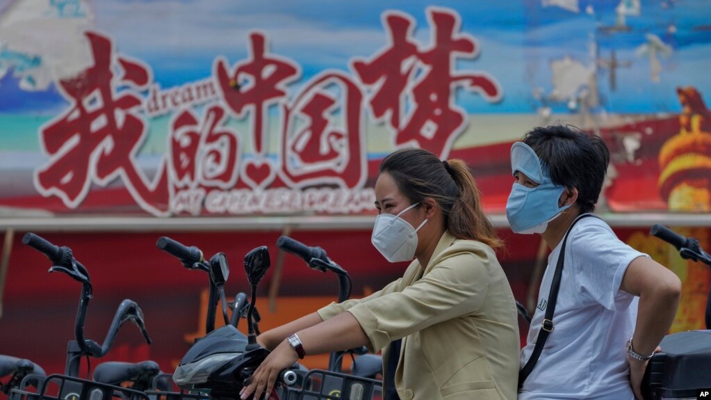 骑着电动车的中国女子驶过中国梦的宣传画。（2022年6月20日）(photo:VOA)