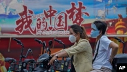 騎著電動車的中國女子駛過中國夢的宣傳畫。（2022年6月20日）