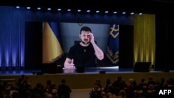 Ukraine's President Volodymyr Zelensky appears on a giant screen as he delivers a statement at the start of a two-day International conference on reconstruction of Ukraine, in Lugano on July 4, 2022. - Ministers from dozens of countries and organisations leaders gathered in Switzerland Monday to hash out a "Marshall Plan" to rebuild the war-torn country. (Photo by Fabrice COFFRINI / AFP)