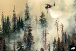 Seen from Mariposa County, California, a helicopter drops water on the Washburn Fire burning in Yosemite National Park, July 9, 2022.
