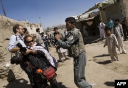 FILE - An Afghan policeman aims his weapon at photojournalists Paula Bronstein, 2nd left, and Kevin Frayer as he prevents them from approaching the area where three gunmen stormed a bank in Kabul, Aug. 19, 2009.