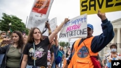 2022年5月14号，支持和反对妇女堕胎权利的美国民众聚集在美国最高法院外举行抗议活动。一名支持堕胎权利的女士试图用手里的标语牌遮盖她身旁一位反对堕胎的抗议人士手中的标语板。-照片来自美联社