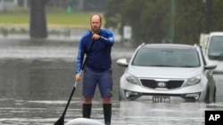 A man paddles on a stand-up paddle board through a flooded street at Windsor on the outskirts of Sydney, Australia, on July 5, 2022. Hundreds of homes have been inundated in and around Australia's largest city in a flood emergency that was impacting 50,000 residents in Sydney.