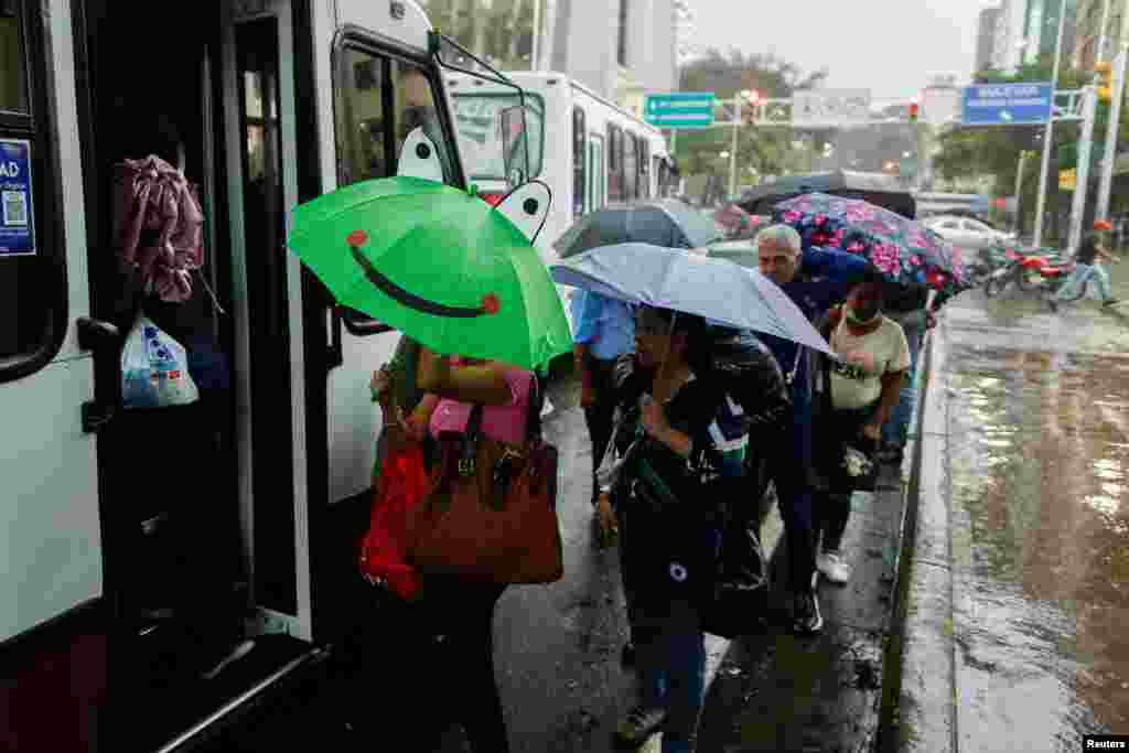 Personas en una fila para abordar un autobús usan paraguas para protegerse de la lluvia.