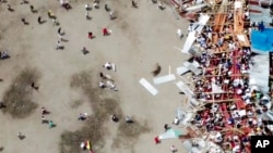 En esta imagen tomada de un video, un hombre, en el centro, intenta llamar la atención de un toro cuando parte de una grada de madera se derrumba durante una corrida de toros, el 26 de junio de 2022, en El Espinal en el estado de Tolima, centro de Colombia.