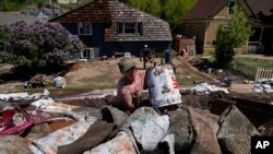 Alecia Halona dumps a bucket of debris into a trailer Wednesday, June 15, 2022, in Red Lodge, Mont. She responded to an online posting requesting help to clean out houses on a street that flooded when torrential rains swelled waterways across the Yellowst