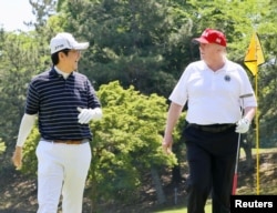 FILE - U.S. President Donald Trump talks with then-Japanese Prime Minister Shinzo Abe as they play golf at Mobara Country Club in Mobara, Chiba prefecture, Japan, in this photo released by Japan's Cabinet Public Relations Office via Kyodo, May 26, 2019.