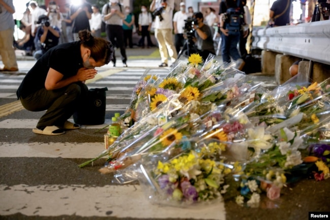 A person prays next to flowers laid at the site where late former Japanese Prime Minister Shinzo Abe was shot while campaigning for a parliamentary election, near Yamato-Saidaiji station in Nara, western Japan, July 8, 2022. (REUTERS/Issei Kato)