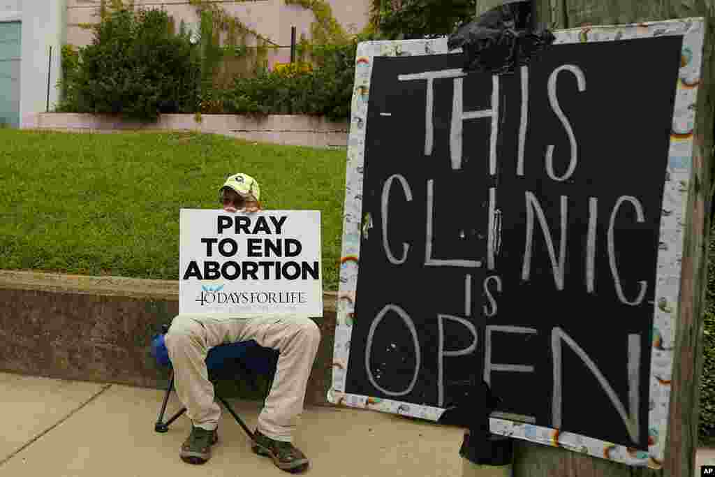 An anti-abortion supporter sits behind a sign that advises the Jackson Women&#39;s Health Organization clinic is still open in Jackson, Mississippi. A state law banning most abortions means the clinic will close at the end of business Wednesday and the state law will take effect Thursday.