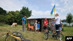 A woman speaks to children in front of a toy cabin made of used ammunition crates in the village of Novoselivka, outside Chernigiv, on June 21, 2022, amid the Russian invasion of Ukraine.
