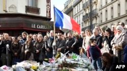 FILE - People observe a minute of silence on Nov. 16, 2015 at the Le Carillon cafe in Paris to pay tribute to victims of the attacks claimed by Islamic State on Nov. 13.
