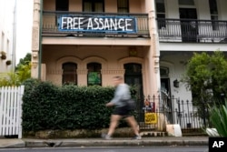 Seorang pejalan kaki berjalan melewati sebuah rumah yang memasang spanduk dukungan untuk pendiri WikiLeaks Julian Assange di Sydney, Australia, Senin, 20 Juni 2022. (AP Photo/Mark Baker)