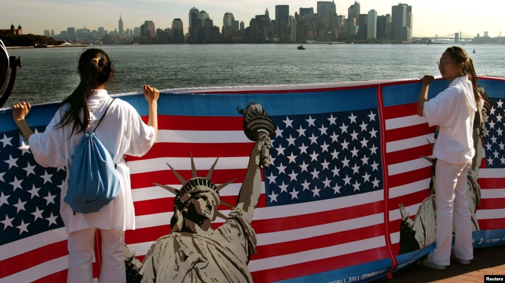 资料照：两名华人女子在纽约手举自由女神像与美国国旗的横幅。(photo:VOA)