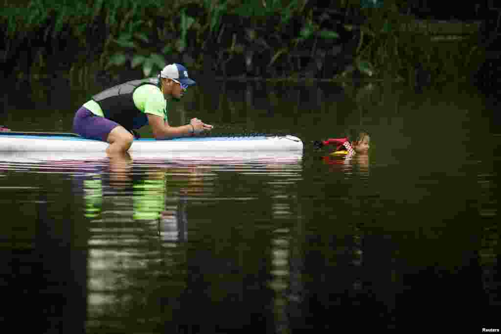 A man assists a girl as she swims in a canal on a hot day of the Summer Solstice in Beijing, China.