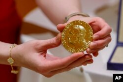 A worker holds Russian journalist Dmitry Muratov's 23-karat gold medal of the 2021 Nobel Peattce Prize before being auctioned at the Times Center, Monday, June 20, 2022, in New York. (AP Photo/Eduardo Munoz Alvarez)