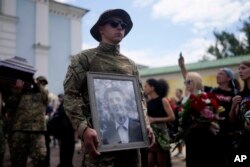 A soldier holds a picture of activist and soldier Roman Ratushnyi during a memorial service in Kyiv, Ukraine, June 18, 2022. Ratushnyi died in a battle near Izyum, where Russian and Ukrainian troops are fighting for control of the area.
