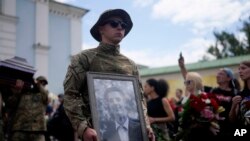 Seorang tentara memegang foto aktivis Roman Ratushnyi dalam upacara pemakaman di Kyiv, Ukraina, Sabtu, 18 Juni 2022. Ratushnyi tewas dalam pertempuran dekat Izyum, di mana pasukan Rusia dan Ukraina memperebutkan kontrol atas wilayah tersebut. (Foto: AP Photo/Natacha Pisarenko)
