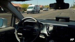 FILE - In this April 7, 2021 file photo, a Waymo minivan moves along a city street as an empty driver's seat and a moving steering wheel drive passengers during an autonomous vehicle ride in Chandler, Arizona.