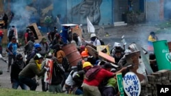 Los manifestantes se protegen detrás de escudos improvisados ​​durante los enfrentamientos con la policía en el centro de Quito, el 24 de junio de 2022.