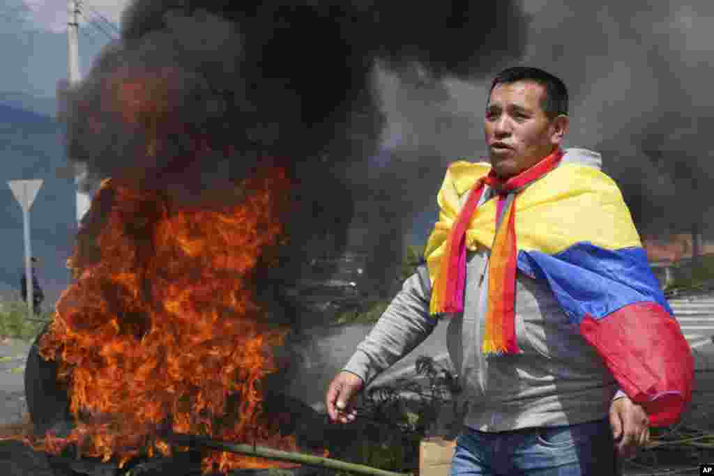 Un manifestante envuelto en una bandera ecuatoriana protesta junto a una barricada en llamas durante una protesta contra el gobierno de Guillermo Lasso convocada principalmente por organizaciones indígenas, en Santa Rosa, Ecuador, el martes 14 de junio de 2022. (Foto AP/Dolores Ochoa)