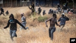 File: Migrants run on Spanish soil after crossing the fences separating the Spanish enclave of Melilla from Morocco in Melilla, Spain, 6.24.2022