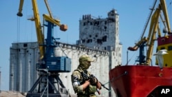 FILE - A Russian soldier guards a pier with the grain storage in the background at an area of the Mariupol Sea Port which has recently started its work after heavy fighting in Mariupol, on the territory which is under the Government of the Donetsk People'