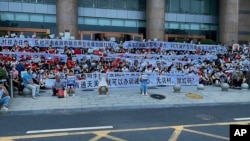 Sejumlah peserta aksi demo membentangkan spanduk dan meneriakan yel-yel dalam aksi protes di depan sebuah kantor cabang Bank Sentral China di Zhengzhou, Henan, pada 10 Juli 2022. (Foto: AP via Yang) 