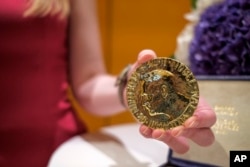 A worker holds Russian journalist Dmitry Muratov's 23-karat gold medal of the 2021 Nobel Peace Prize before being auctioned at the Times Center, Monday, June 20, 2022, in New York.