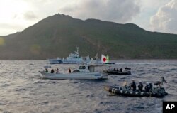 Kapal dan perahu Penjaga Pantai Jepang, belakang dan kanan, berlayar di samping perahu nelayan aktivis Jepang, berbendera tengah, dekat gugusan pulau yang disengketakan yang disebut Diaoyu oleh China dan Senkaku oleh Jepang, 18 Agustus 2013. (Foto: AP )