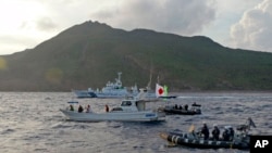 FILE - Japanese Coast Guard vessel and boats, rear and right, sail alongside a Japanese activists' fishing boat, center with a flag, near a group of disputed islands called Diaoyu by China and Senkaku by Japan, Aug. 18, 2013.