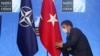 Seorang petugas membetulkan letak bendera Turki yang berdampingan dengan bendera NATO pada KTT NATO di Brussels, 14 Juni 2021. (Foto: via AP)