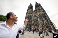 Fadel Alkhudr dari Syria berpose di dekat kata heritage Cologne Cathedral di Cologne, Jerman, Senin, 20 Juni 2022. (Foto: AP)