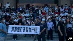 Varias personas sosteniendo letreros y coreando consignas en una protesta afuera de una sucursal del banco central de China, en Zhengzhou, en la provincia de Henan, en el centro de China. (AP Foto/Yang)