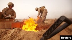 FILE - U.S. Marines dispose of trash in a burn pit while stopping for a sandstorm to pass during a convoy to Patrol Base Sre Kalad in Khan Neshin District, Afghanistan March 3, 2012. 