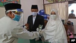 Pasangan di Pamulang, Tangerang Selatan, menerima buku nikah dari seorang penghulu dalam pernikahan mereka yang digelar di tengah perebakan pandemi COVID-19 pada 19 Juni 2022. (Foto: AP/Tatan Syuflana)