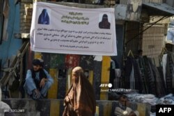 Seorang perempuan yang menggunakan burqa berjalan melewati spanduk yang dipasang oleh otoritas Taliban yang meminta perempuan untuk mengenakan jilbab, di Kandahar pada 16 Juni 2022. (Foto: AFP/Javed Tanveer)