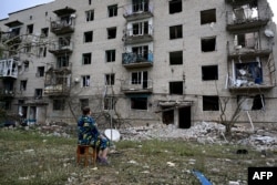A woman sits in front of her building, which has been partially destroyed after a Russian missile hit the a four-story residential building in Chasiv Yar, Donetsk region, eastern Ukraine, July 10, 2022.