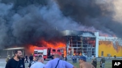 La gente observa cómo el humo brota después de que un ataque con misiles rusos golpeó un centro comercial lleno de gente, en Kremenchuk, Ucrania, el lunes 27 de junio de 2022.